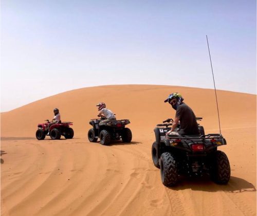 Three riders on desert buggies driving across sand dunes during evening buggy tour